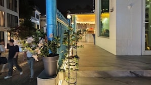 Um edifício com design moderno, apresentando um pilar azul e plantas em vasos ao longo da passarela.