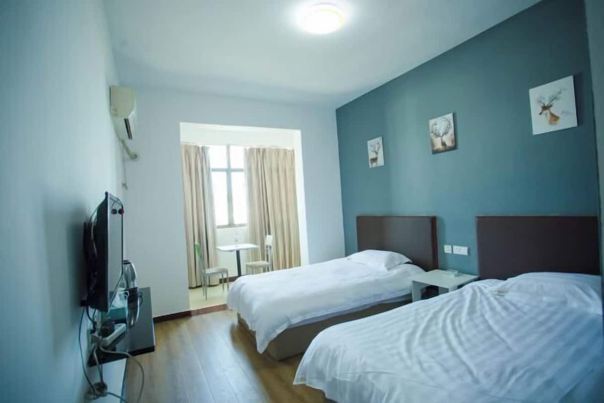 Ένα δωμάτιο ξενοδοχείου με δύο κρεβάτια, μια τηλεόραση και ένα παράθυρο με κουρτίνες.