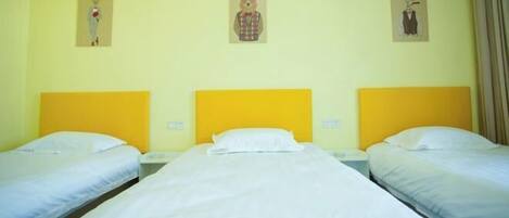 A hotel room with three beds, each with a yellow headboard, white bedding, and a small painting above each bed.