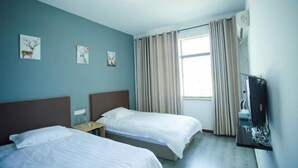 A hotel room with two single beds, a nightstand, a TV, and a window with curtains.