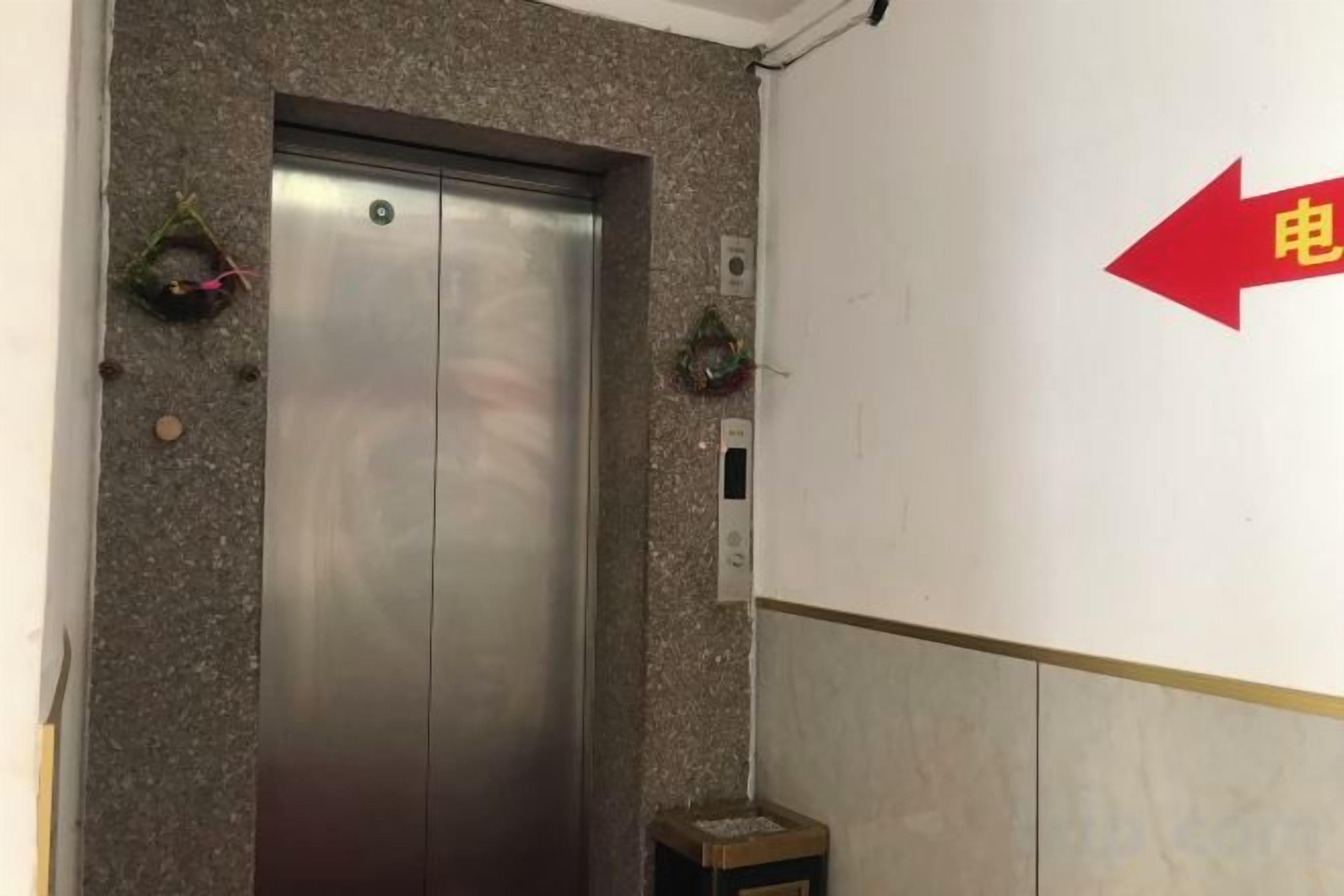 An elevator with a metallic finish, a wall-mounted electrical outlet, and a directional arrow sign.