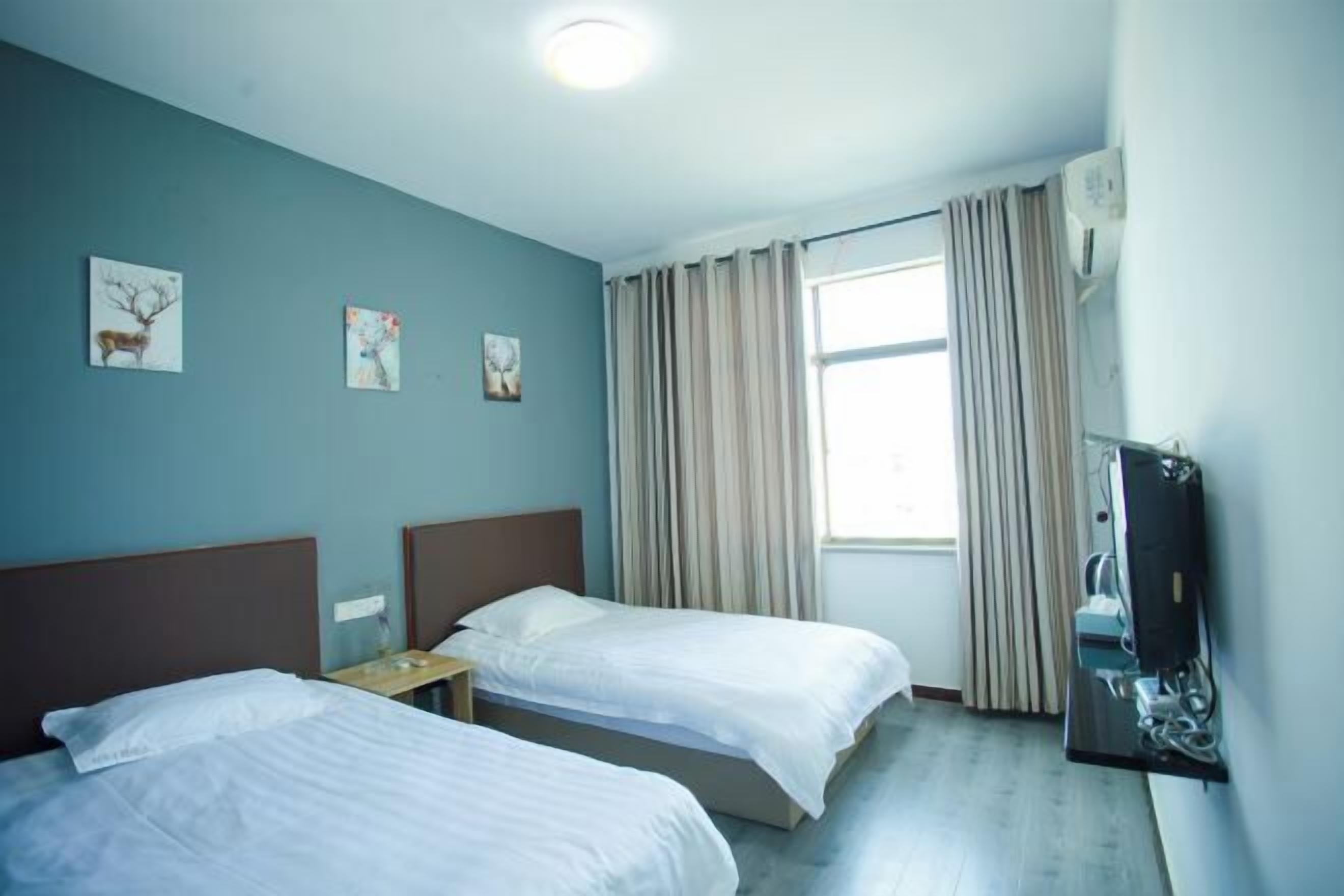 Hotellihuone, jossa on kaksi sänkyä, televisio ja ikkuna, jossa on verhot.
