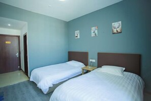 Quarto de hotel com duas camas, uma porta de madeira e três quadros pendurados na parede.
