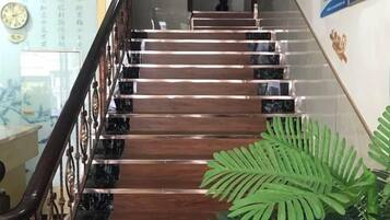 A staircase with a black and wood finish, a metal railing, and a green plant at the bottom.