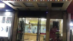 A hotel entrance with a reception desk, glass doors, and a check-in counter.