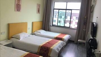 A hotel room with three beds, a window with curtains, a television, and a coffee maker.