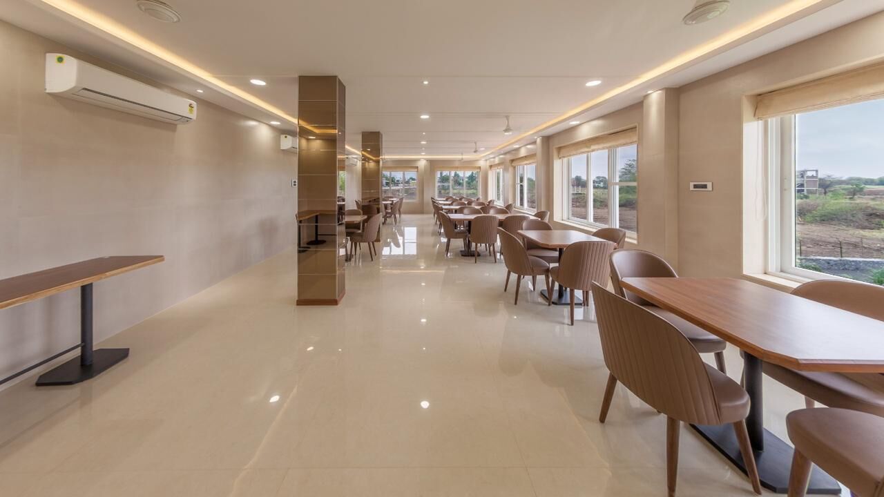 A spacious dining area with long tables and chairs, large windows, and air conditioning units.