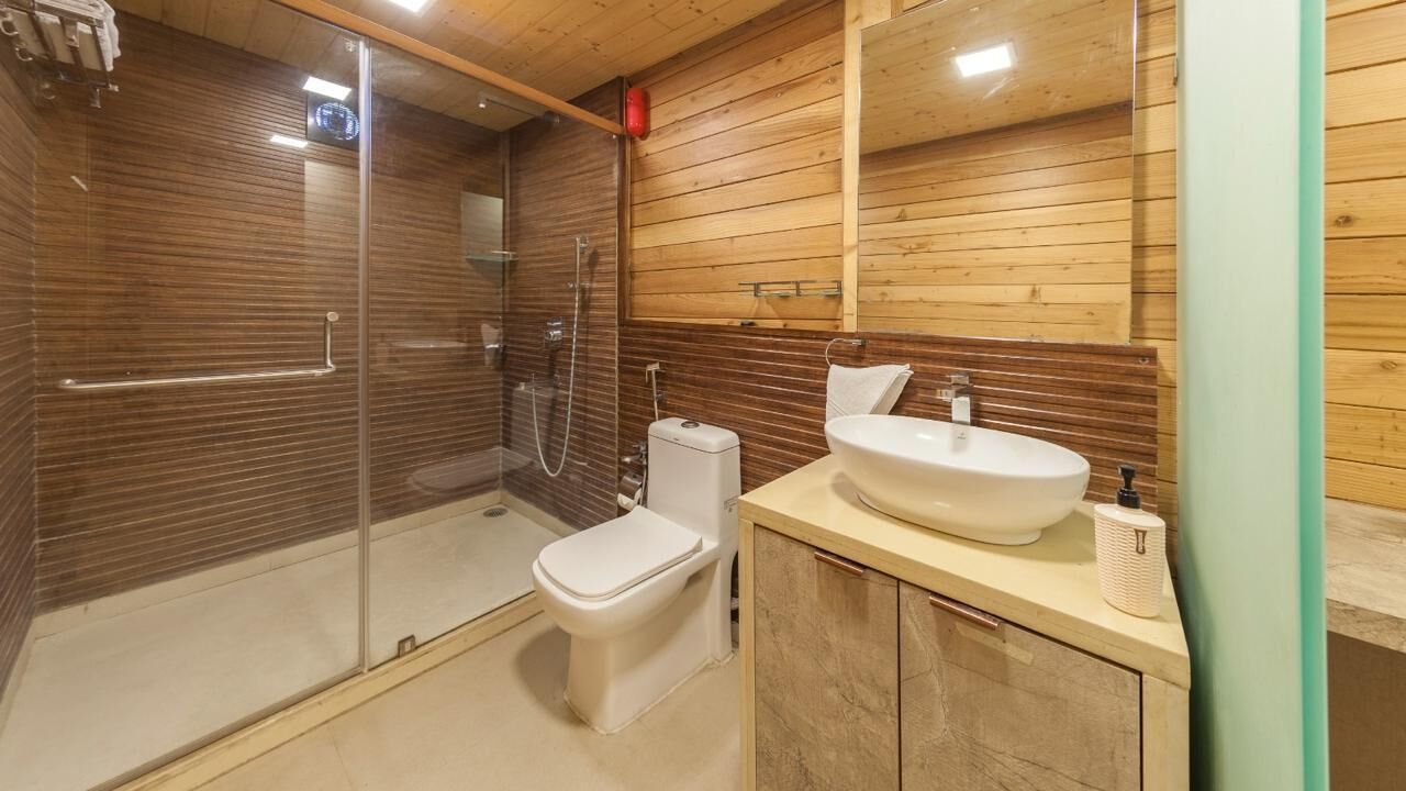 Et moderne badeværelse med en brusekabine i glas, et hvidt toilet og en håndvask med et spejl over.