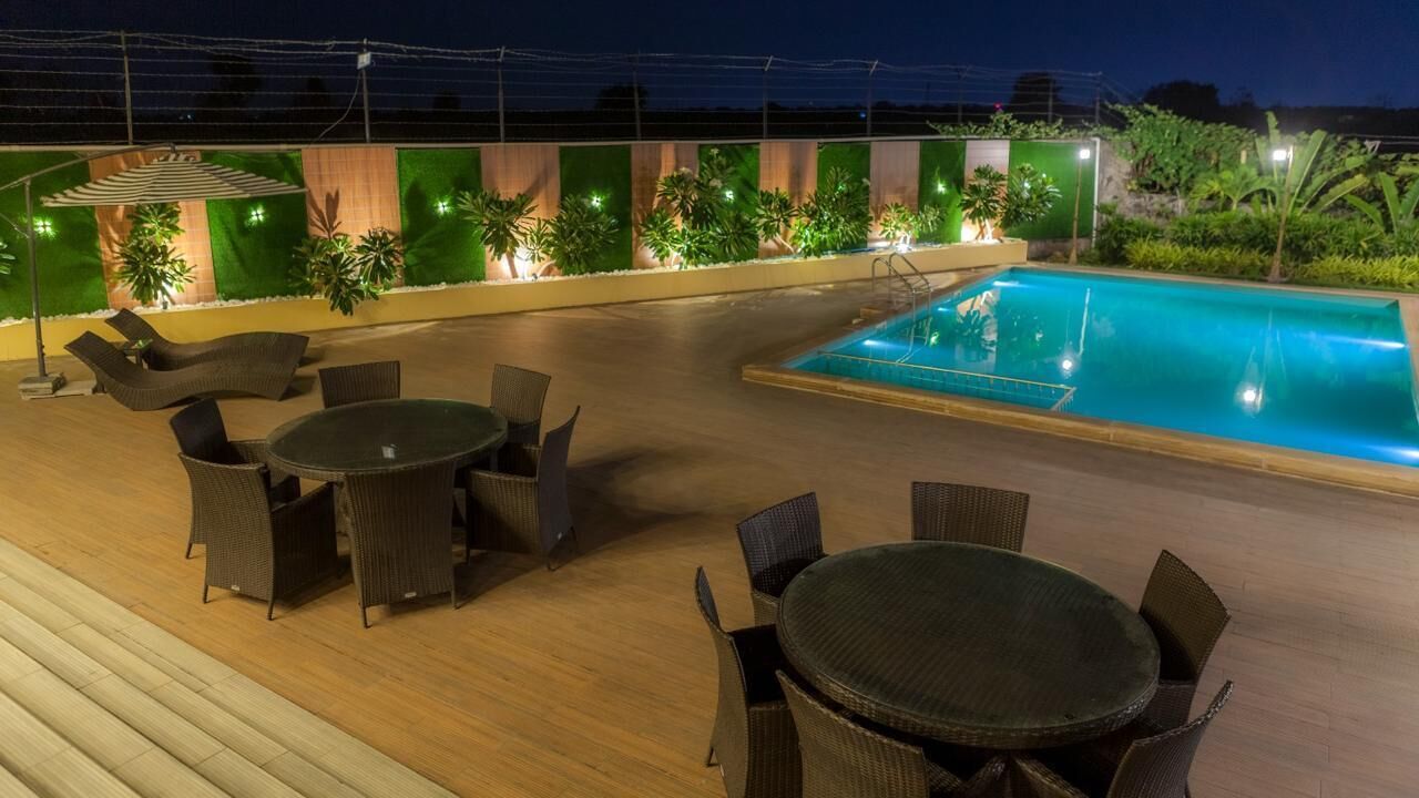 A rooftop pool area with lounge chairs and tables, surrounded by greenery and a wooden deck.