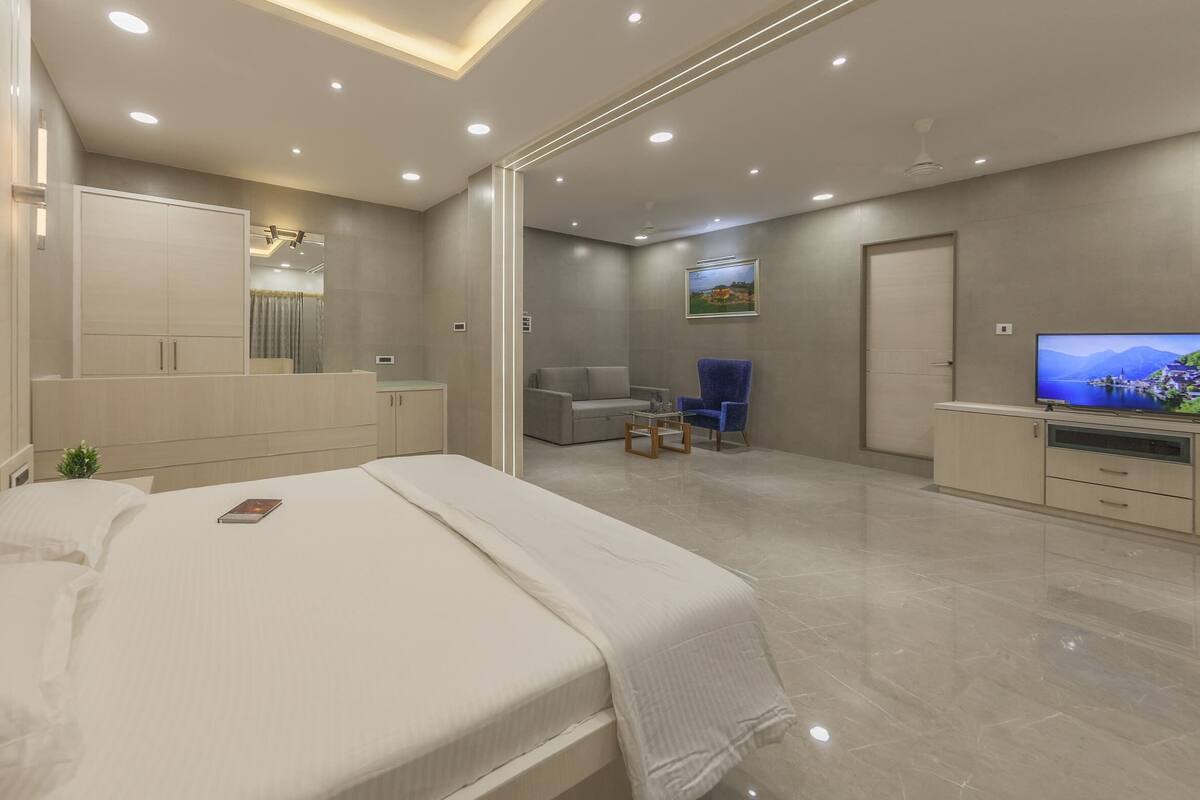 A modern bedroom with a large bed, a TV, and a seating area with a sofa and armchair.