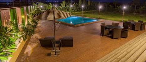 An outdoor pool area with a wooden deck, lounge chairs, and a small table.