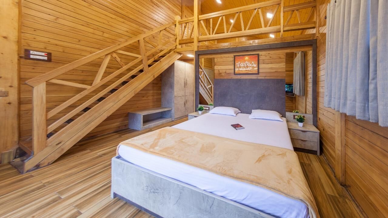 Un dormitorio de cabaña de madera con una cama, mesitas de noche, un cuadro enmarcado y una escalera.