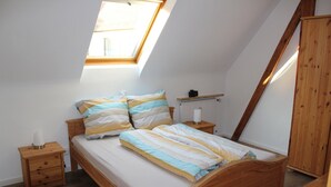 A bedroom with a sloped ceiling, a skylight, a wooden bed, a nightstand, a radiator, and a wardrobe.