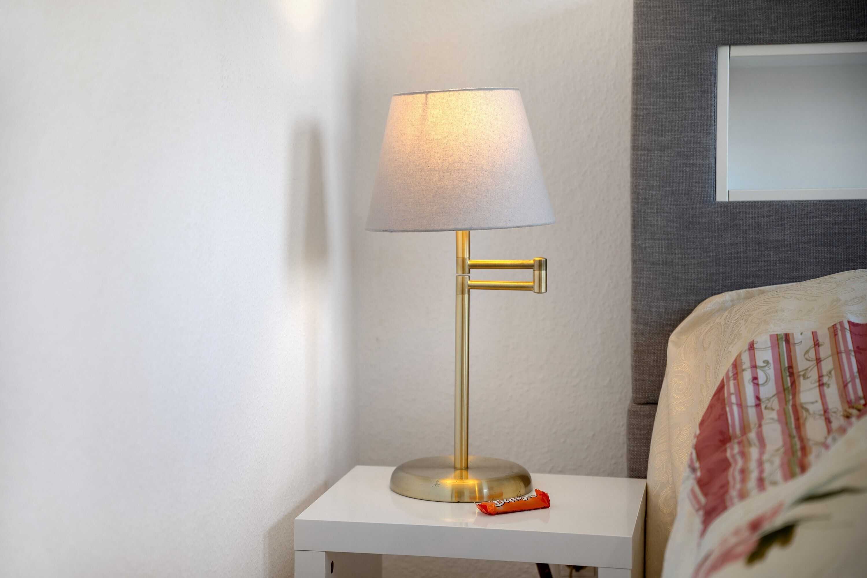 Ein Nachttisch mit einer Lampe, einem Kopfkissen und einem kleinen Gegenstand darauf.