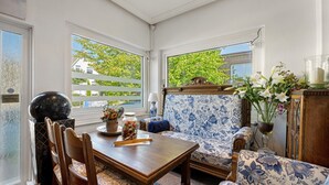 A corner room with a dining table, chairs, a sofa, and a window with a view of greenery.