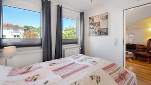A bedroom with a bed, a window with curtains, a radiator, a lamp, and a wall with a poster.