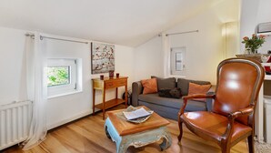 A living room with a sofa, a wooden coffee table, a leather armchair, a window with curtains, and a painting on the wall.