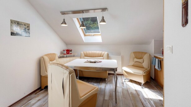 A room with a sloped ceiling, a skylight, a table with chairs, and a radiator. - Apartment 'Fewo Mit Balkon Am Wald 2-4 Pers' with Mountain View, Private Garden and Wi-Fi (Bad Sachsa)