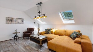 A loft-style room with a large window, a brown leather sofa, a small round table, and a hanging light fixture. - Apartment 'Fewo Mit Balkon Am Wald 2-4 Pers' with Mountain View, Private Garden and Wi-Fi (Bad Sachsa)