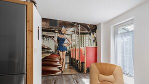 A room with a large mirror reflecting a person in a blue dress, a wooden-framed door, a stainless steel refrigerator, a window with sheer curtains, and a brown leather chair. - Apartment 'Fewo Mit Balkon Am Wald 2-4 Pers' with Mountain View, Private Garden and Wi-Fi (Bad Sachsa)