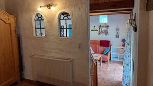 Un corridoio con un termosifone, una porta in legno e vista su un soggiorno con un divano e un tavolo.