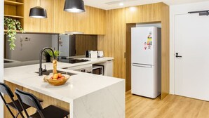 Eine moderne Küche mit Holzsäulen, einem weißen Kühlschrank und einer zentralen Kochinsel mit einer Obstschale.