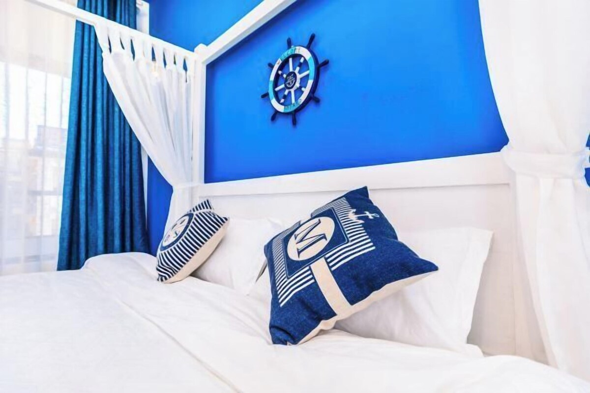 Una cama con ropa blanca y dos almohadas, una con diseño náutico y la otra con estampado geométrico.