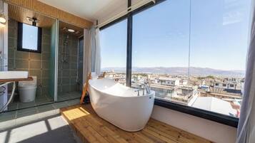 A modern bathroom with a freestanding bathtub, a glass shower enclosure, and a large window offering a city view.