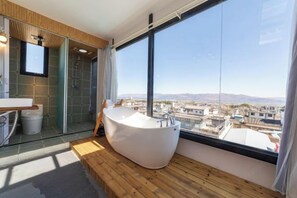 A modern bathroom with a freestanding bathtub, a glass shower enclosure, and a large window offering a city view. - Long Sunshine (Dali City)