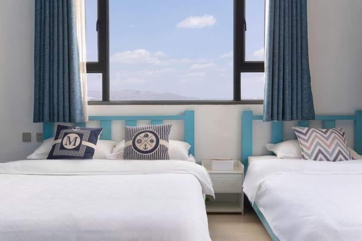 Une chambre d’hôtel avec deux lits, chacun agrémenté d’un oreiller au design différent, une table de chevet et une vue sur le ciel et les montagnes.