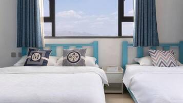 A hotel room with two beds, each with a different pillow design, a nightstand, and a view of the sky and mountains.