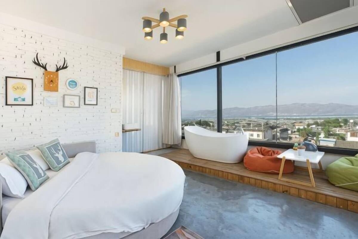 Une chambre moderne avec une grande fenêtre, un lit blanc, une baignoire et une vue sur la ville.