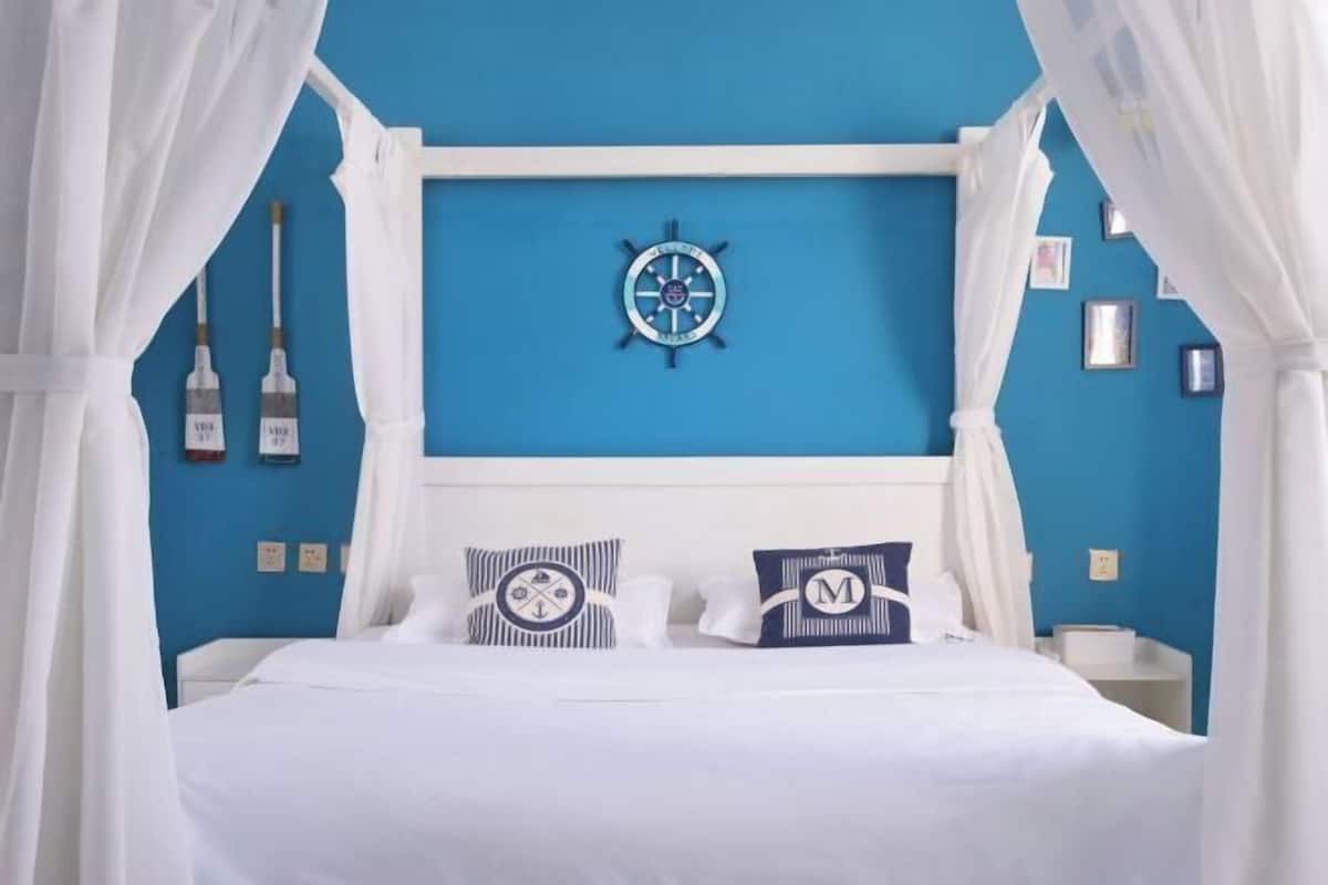 Un lit avec une literie blanche, une horloge murale sur le thème de la marine et deux coussins ornés de motifs d’ancre.