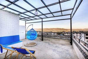 A rooftop terrace with a hanging chair, a cushioned bench, and a view of the cityscape. - Long Sunshine (Dali City)