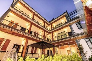Un edificio de varios pisos con balcones, un área de estar al aire libre techada y una fachada bien iluminada.