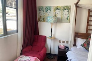 A room with a red chair, a bed with white bedding, a bedside table with a lamp, and a wall with three paintings. - Long Sunshine (Dali City)
