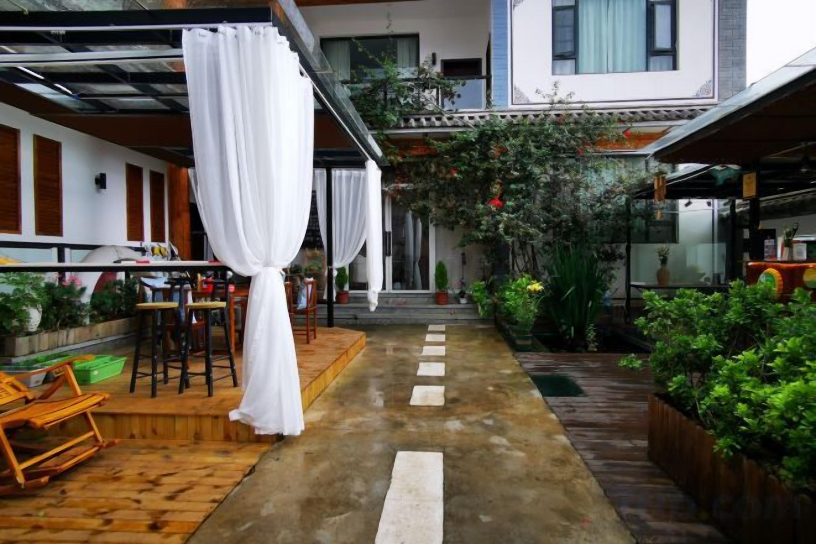 A covered outdoor seating area with tables and chairs, a wooden deck, and a pathway leading to a building entrance.