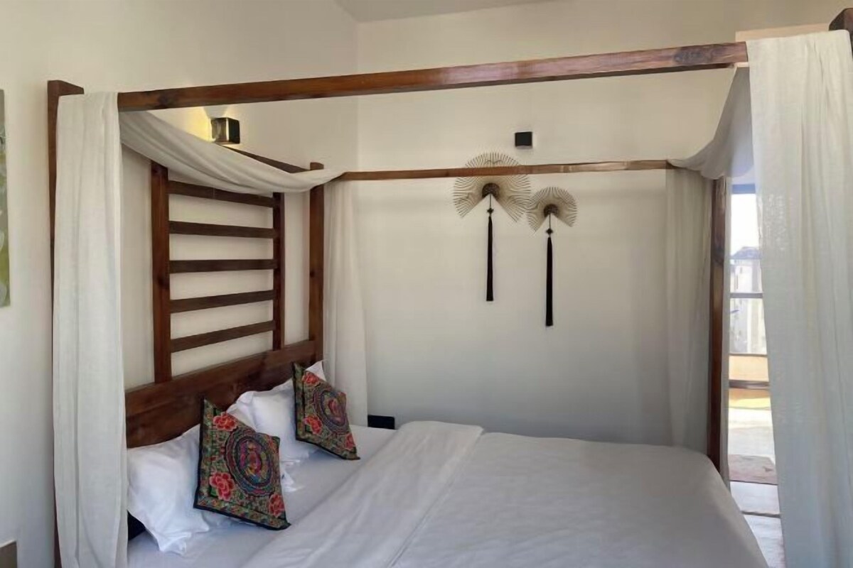 Un dormitorio con cabecera de madera, cama con ropa de cama blanca, almohadas decorativas y un ventilador de pared.
