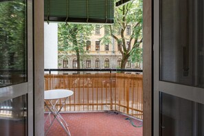 Un balcon donnant sur un immeuble, une table blanche et un sol en briques rouges.