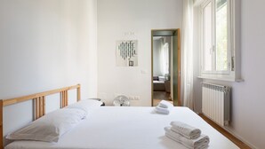 Ein ordentlich bezogenes Bett mit weißen Leinen, einem Holz-Kopfteil und einem Heizkörper an der Wand.