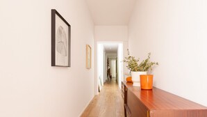 Ein Flur mit Holzboden, einer Holzbank, einer weißen Wand mit einem gerahmten Bild und einem Topfpflanzen.