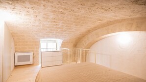 Een slaapkamer met een schuine kap, een bed, een dressoir en een klein raam.