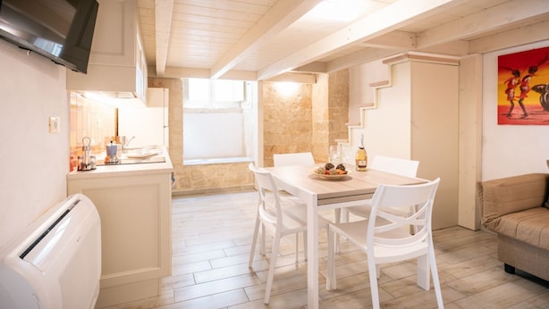 Een eetgedeelte met een tafel en stoelen, een keuken met een fornuis, en een aan de muur bevestigde televisie.