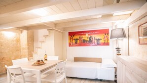 Een kamer met een houten vloer, witte meubels, een schilderij aan de muur en een lamp.
