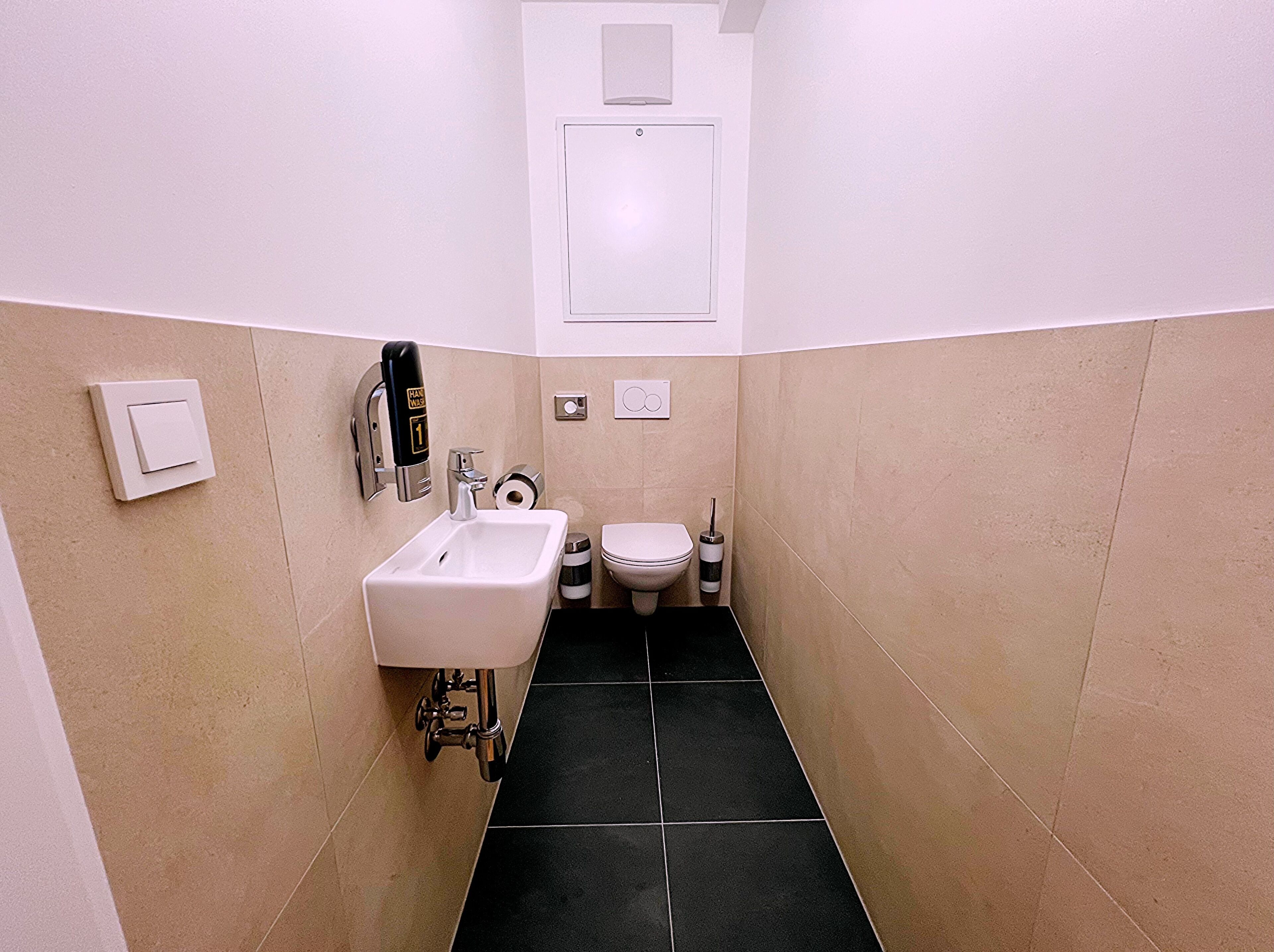 Et lille, smalt badeværelse med hvid vask, toilet og pissoir.