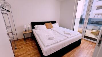 Un dormitorio moderno con una cama grande, una mesita de noche, una lámpara y vistas al exterior a través de un ventanal.