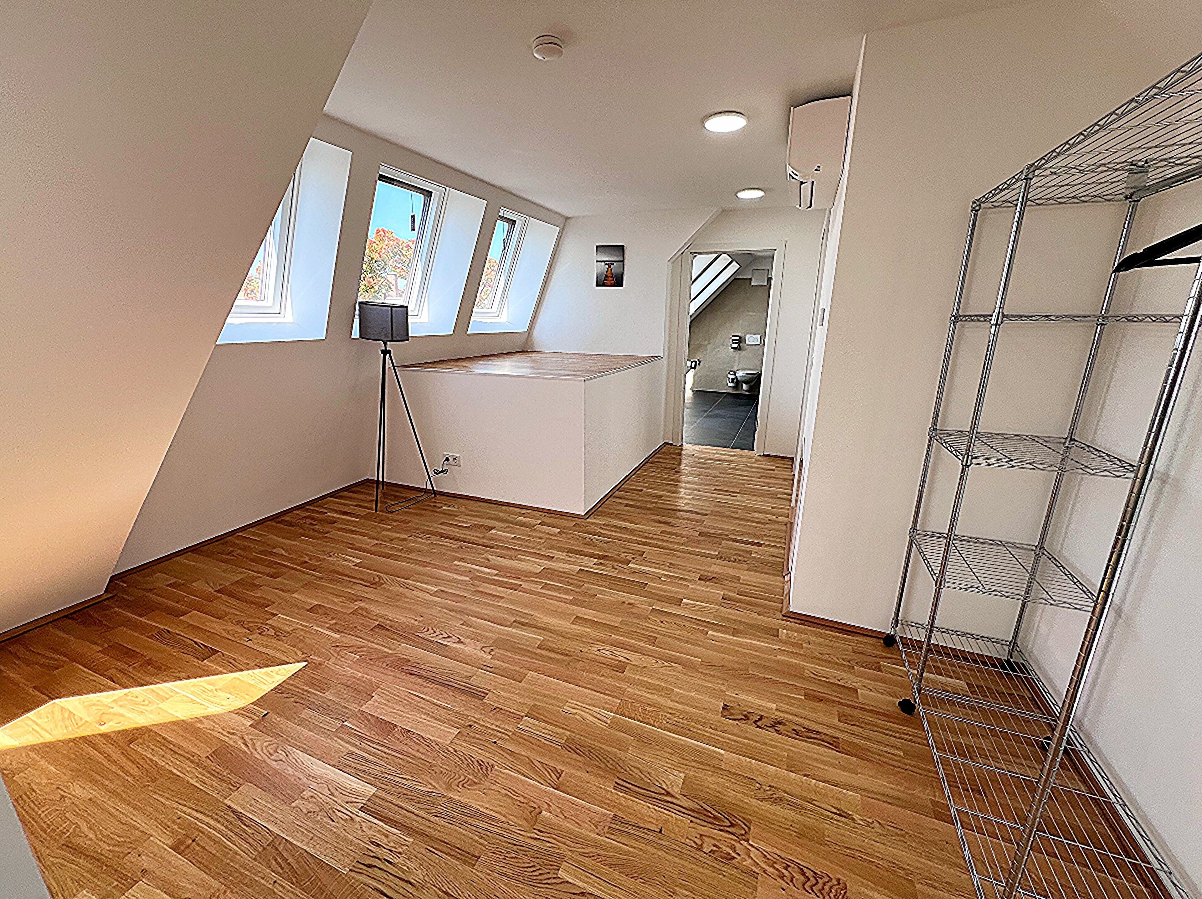 A spacious room with wooden flooring, a kitchenette, and a metal shelving unit.