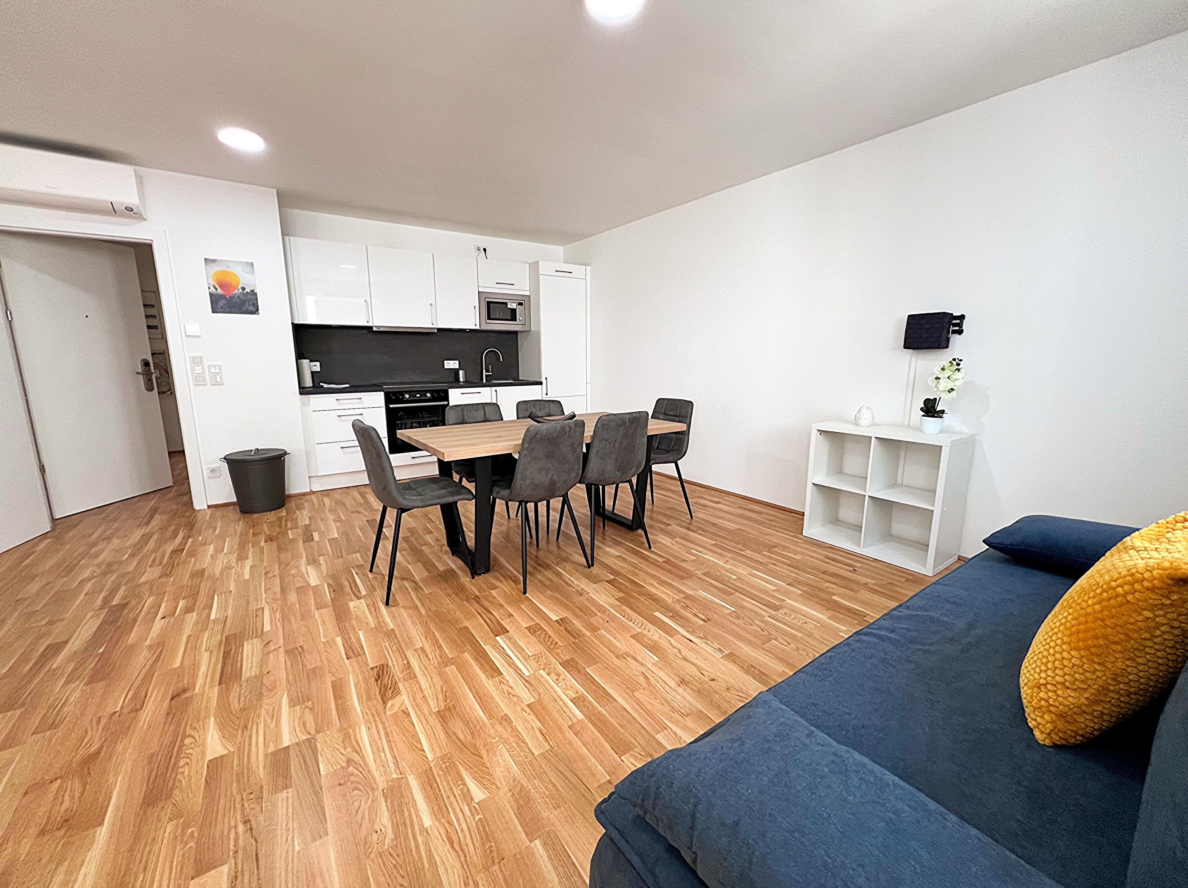 A modern apartment with a dining area, kitchenette, and a living room with a sofa and a small side table.
