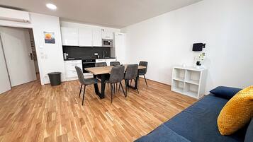 A modern apartment with a dining area, kitchenette, and a living room with a sofa and a small side table.