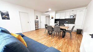 Un salon moderne avec un canapé bleu, une table à manger avec des chaises et un coin cuisine doté de meubles blancs et d’appareils électroménagers.